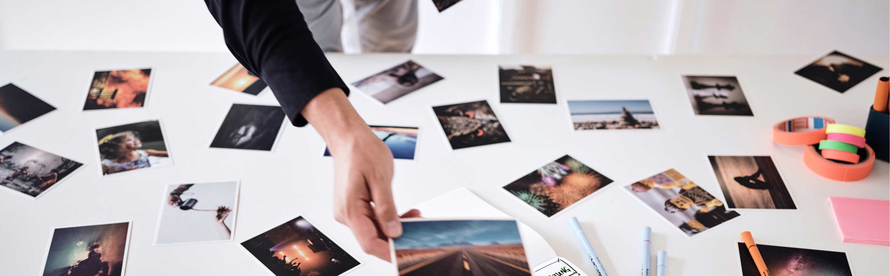 Hand greift nach einem Foto auf einem Tisch voller Polaroid-Fotos